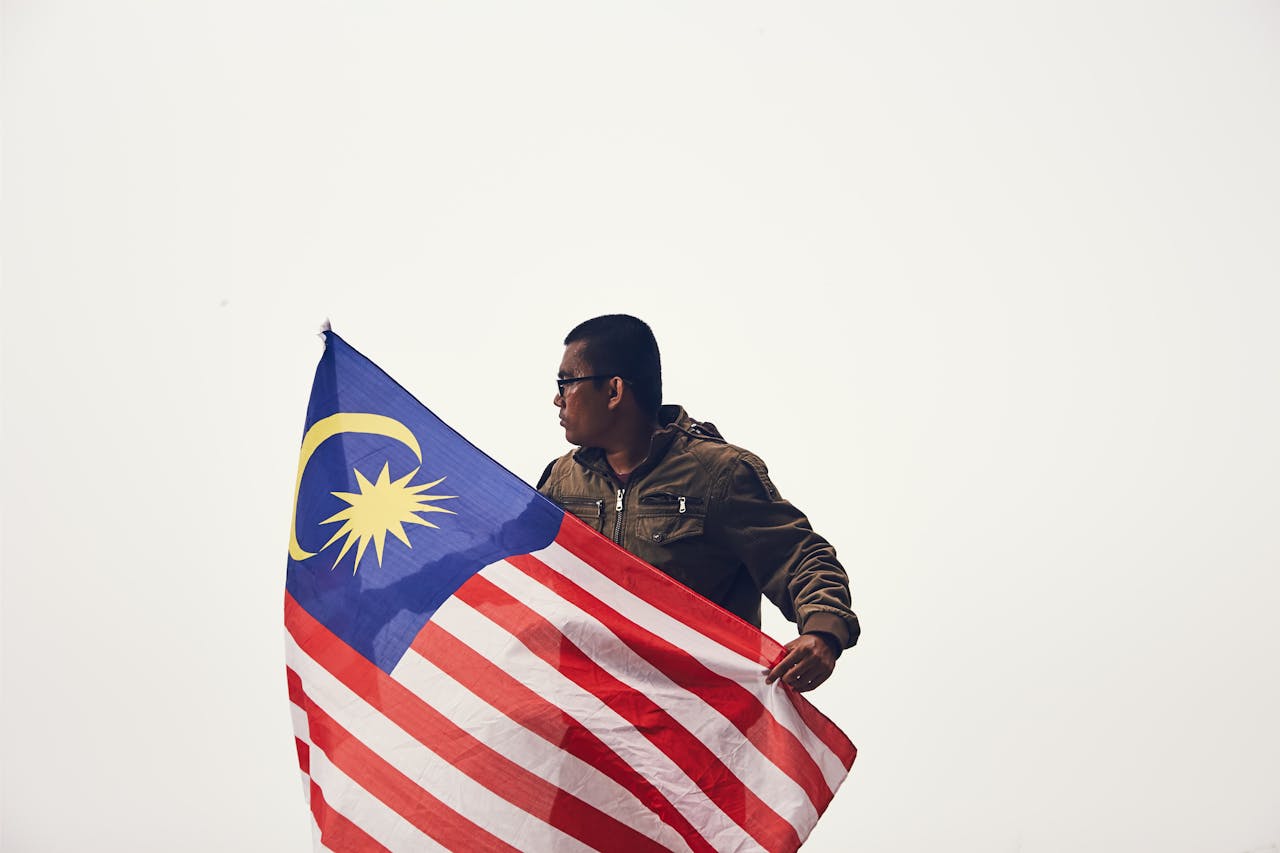 about-us-01 A man proudly holds the Malaysian flag, symbolizing patriotism and national pride.