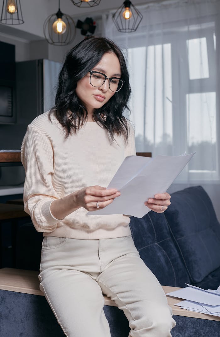 about-us-01 Concentrated young woman with glasses reading financial papers in a modern living room.