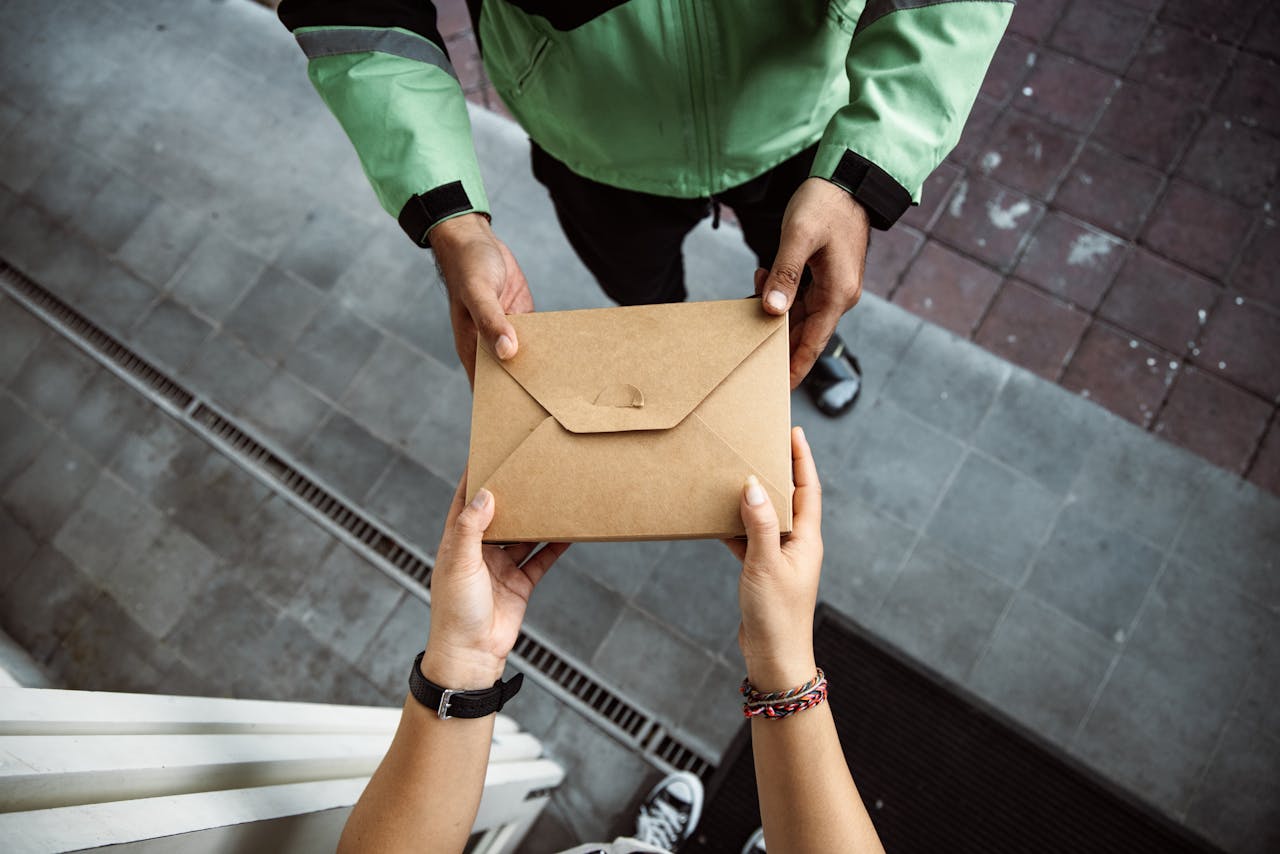 about-us-02 Close-up of hands exchanging a brown envelope outdoors on a pavement scene.